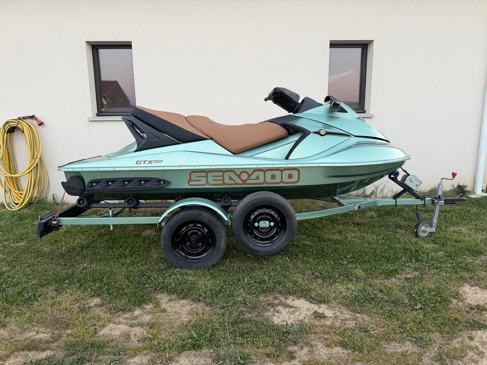 Jet-ski Sea-Doo vert d’eau et brun sur sa remorque, devant l’atelier