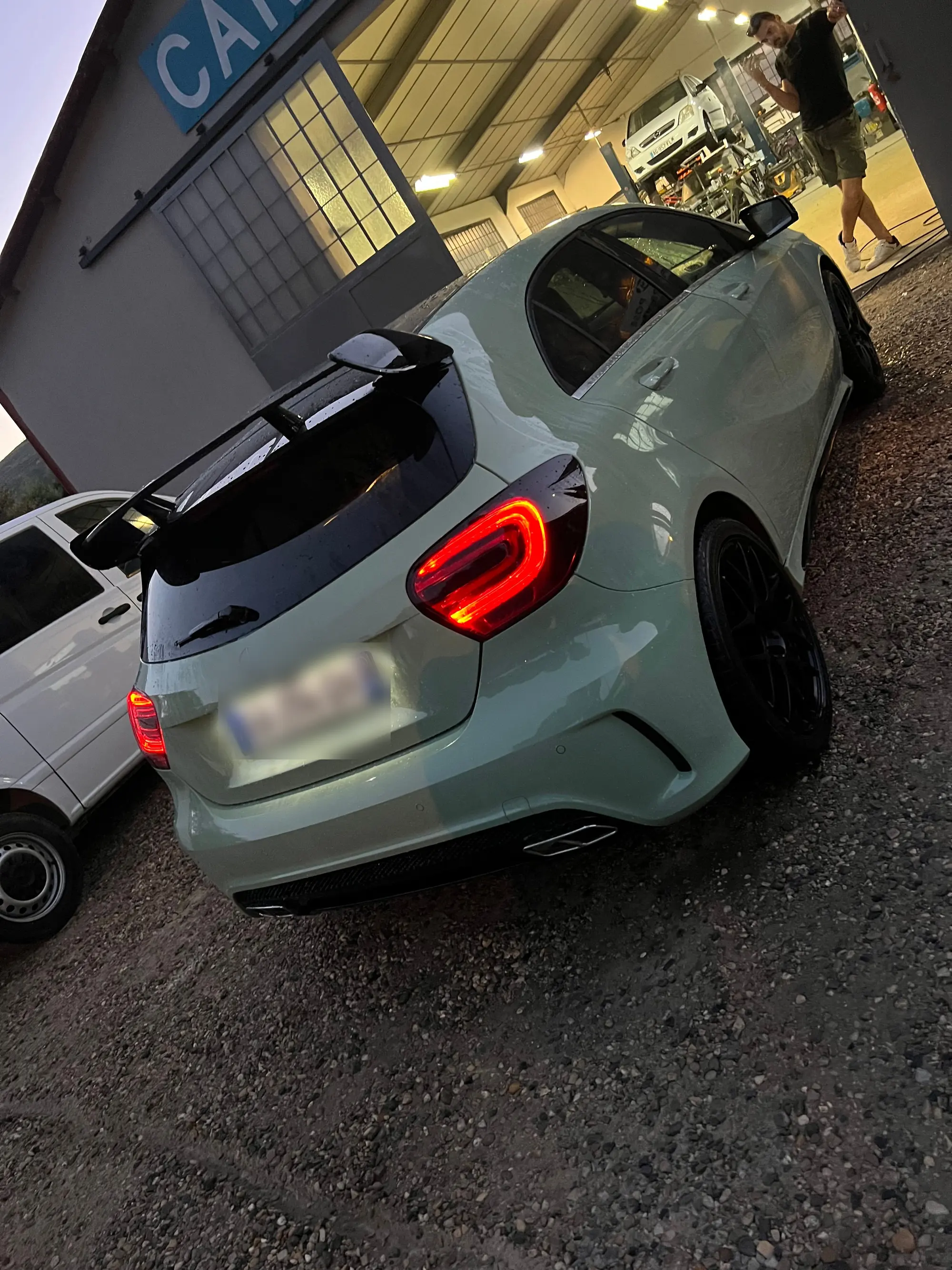 Mercedes Classe A gris clair à béquet noir, garée à la tombée du jour devant l’atelier éclairé