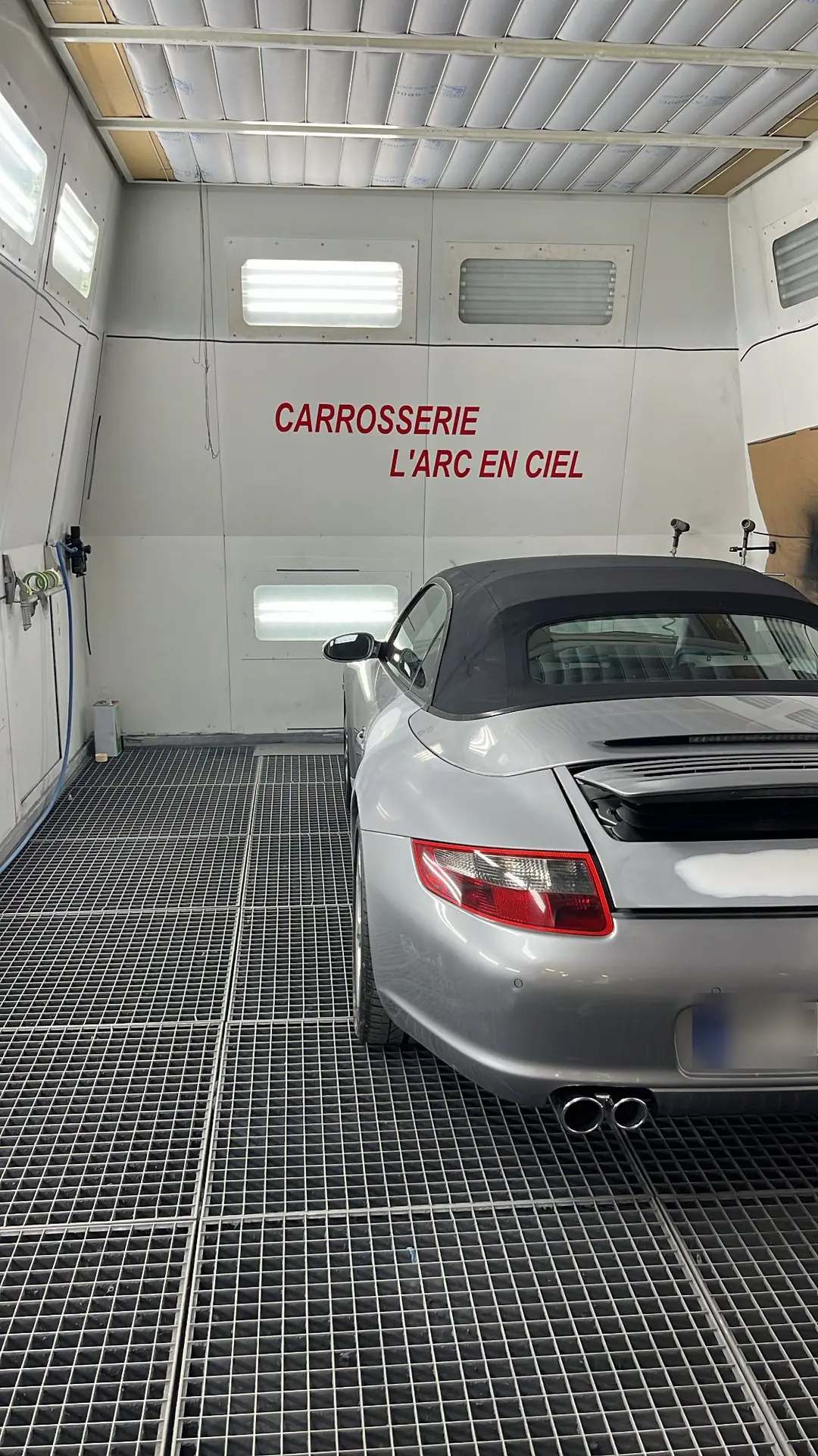 Une Porsche 911 cabriolet grise dans la cabine de peinture de l’atelier, au nom de la Carrosserie L’Arc en Ciel